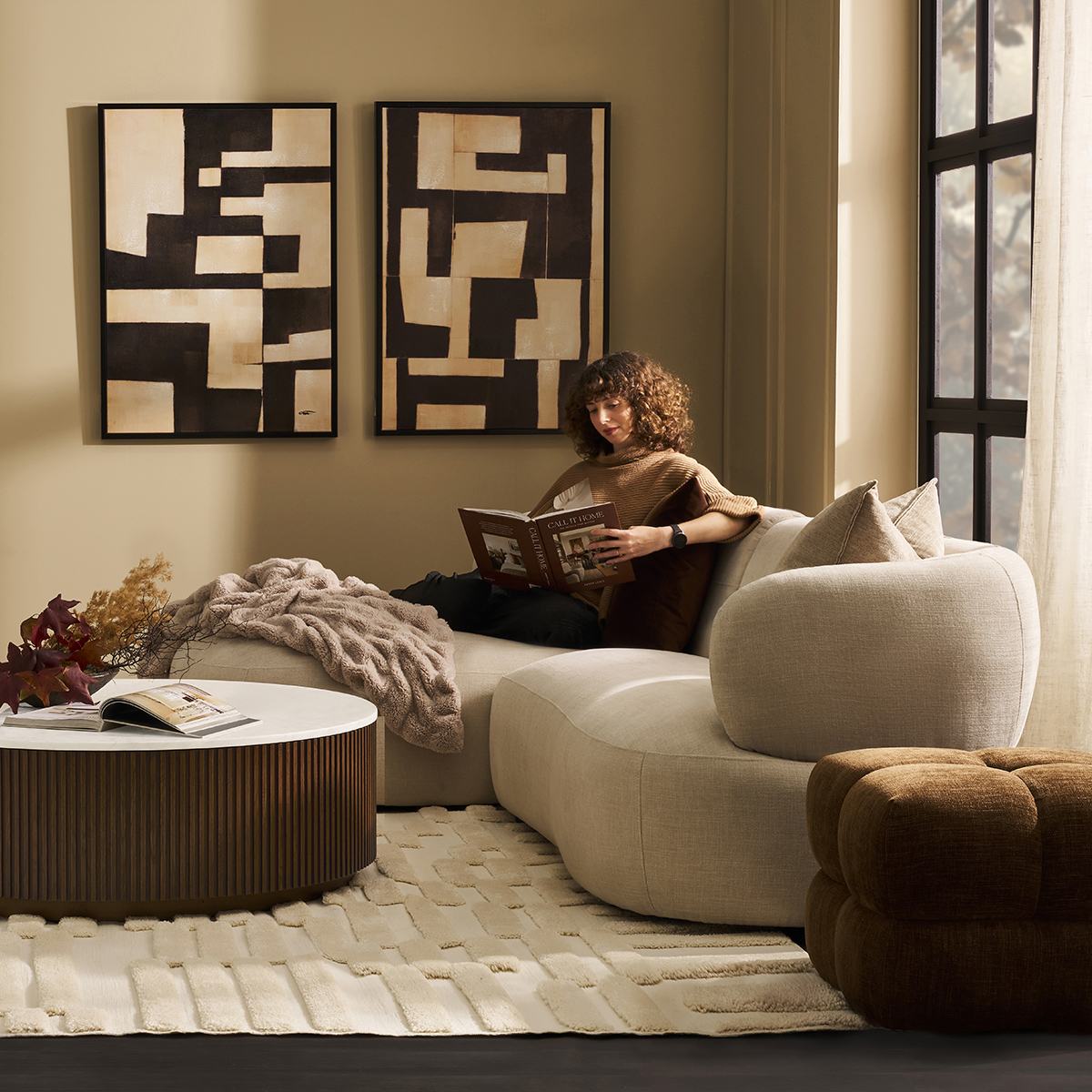 A curved Greenwich modular sofa with chaise, a woman reading beneath bold abstract art
