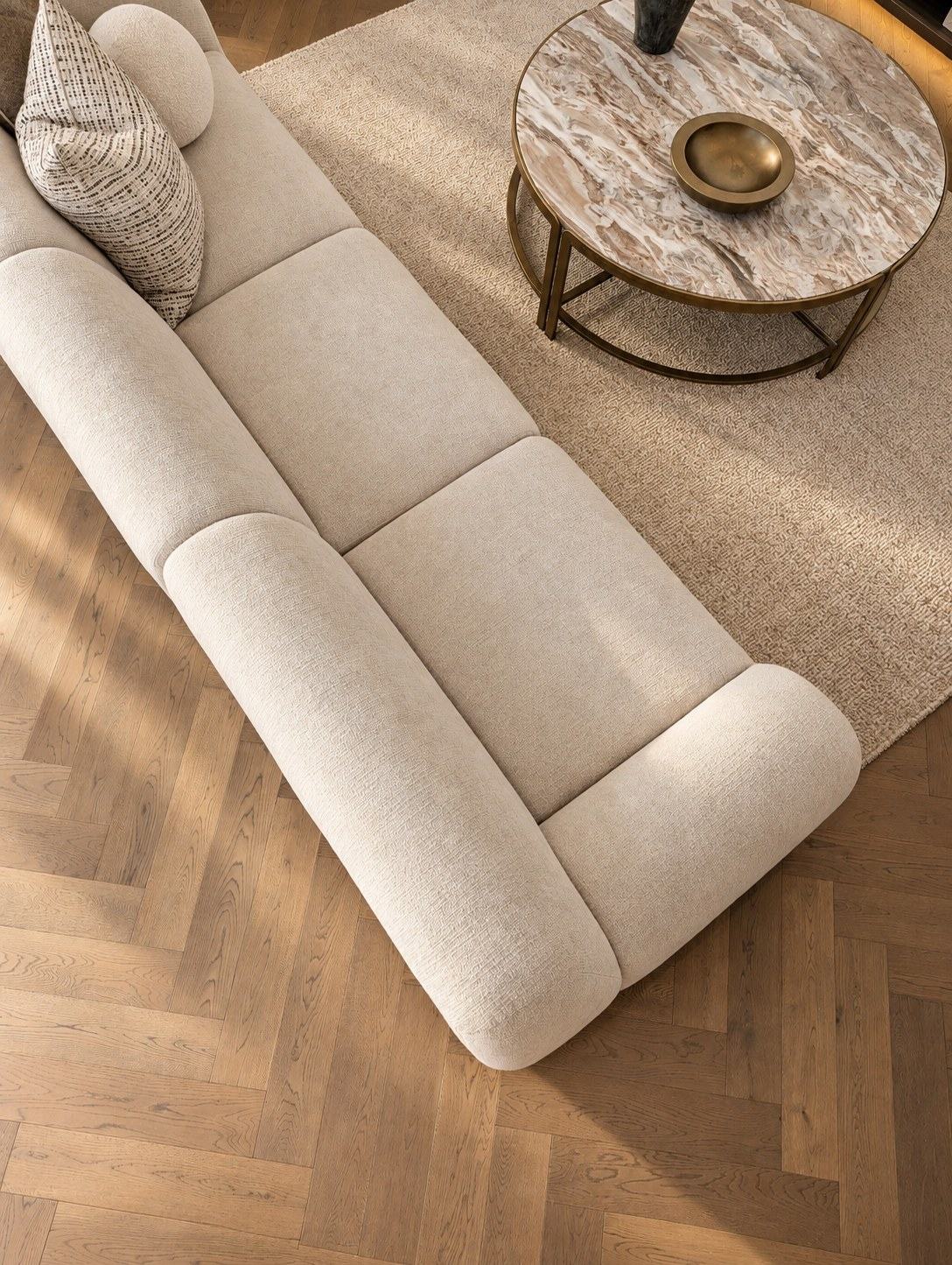 Freya in a textured off white from above, beside a marble and brass coffee table on herringbone oak